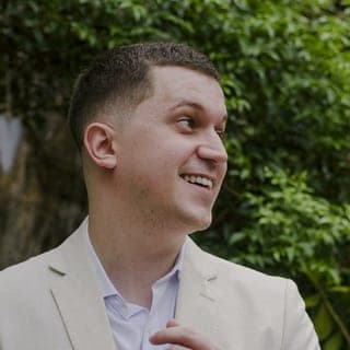 Eduardo Bittencourt, de terno de linho claro, olhando para o lado e sorrindo, em um jardim